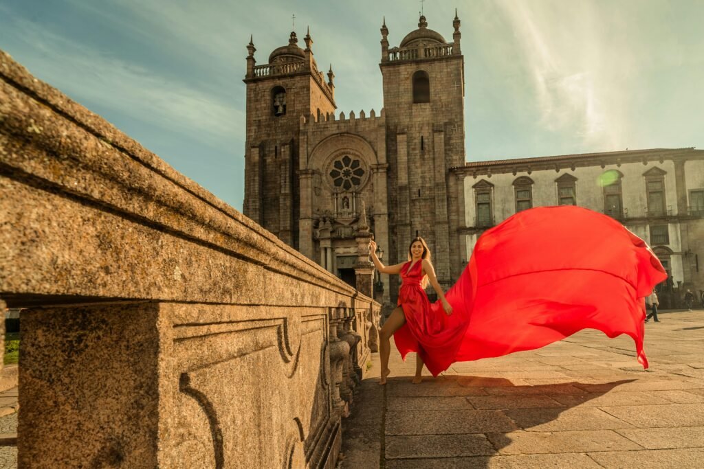 A woman in a red dress poses at Porto Cathedral in Portugal on a sunny day.