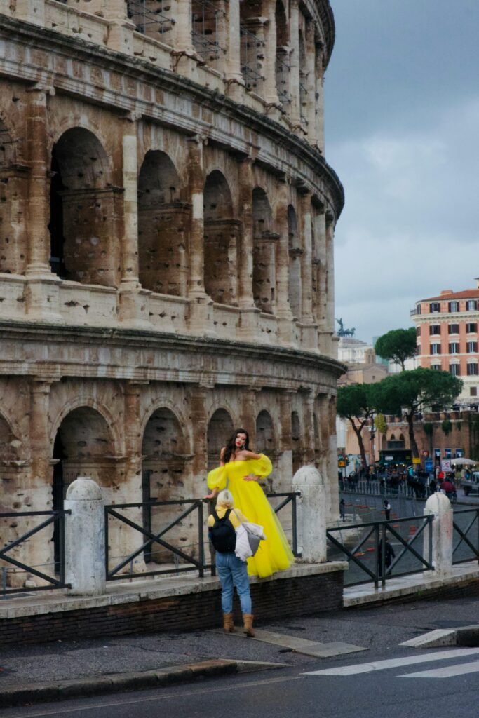 Elegant model in a yellow dress poses by the Colosseum in Rome, capturing a blend of modern fashion and ancient architecture.
